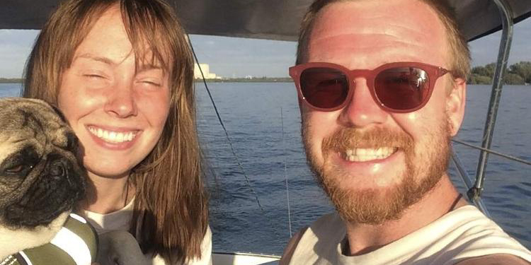 casal aparece ao lado do cachorro sorrindo dentro do barco