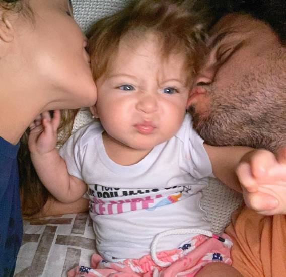 Bela sendo beijada por Claudia Leitte e Marcio Pedreira, seus pais