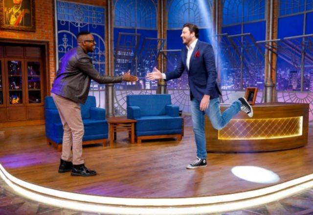 Mumuzinho e Danulo, no cenário do The Noite, se cumprimentam de longe, em pé