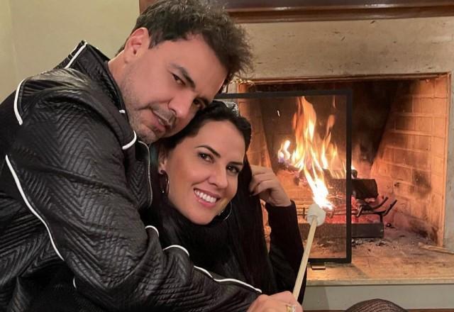 Zezé Di Camargo e Graciele Lacerda abraçados em frente a uma lareira