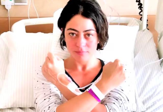 Foto de Carol Castro em cama de hospital fazendo um gesto de X com os braços