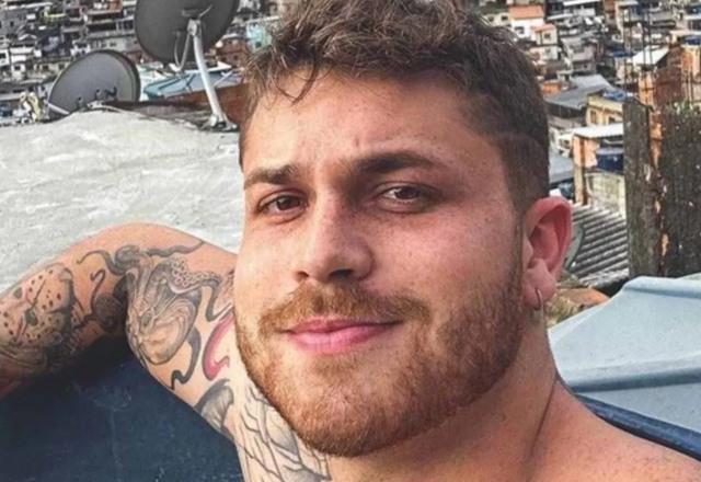 Foto de Gustavo Tubarão olhando para a câmera, sem camisa em um telhado de uma casa de periferia