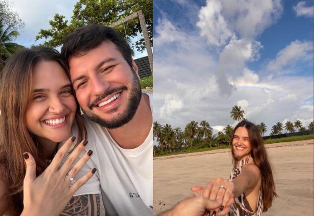 Juliana Paiva exibe aliança de noivado ao lado de Danilo Partezani em praia ao pôr do sol, com arco-íris ao fundo