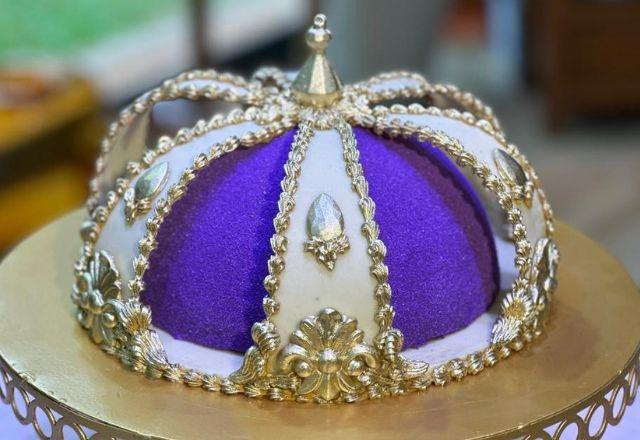 Na foto temos uma Mousse Real em formato de esfera, decorada com tiras de chocolate branco, detalhes dourados e acabamento aveludado em tom roxo.