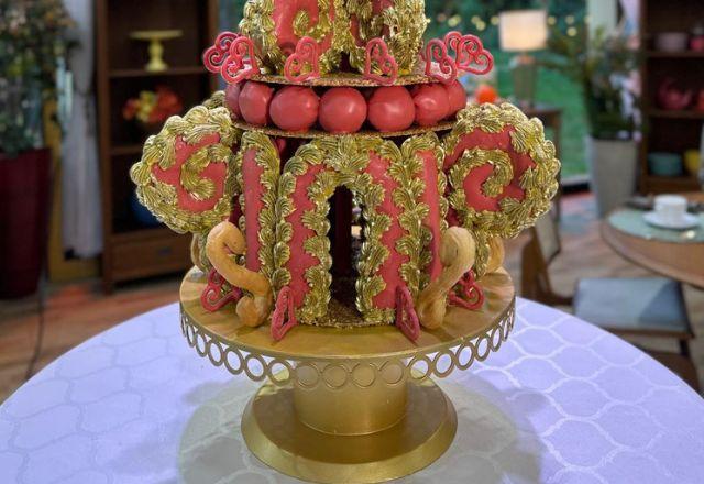 Na foto temos uma torre de massa choux montada em vários andares, decorada com chocolate vermelho, arabescos, detalhes em dourado e carolinas recheadas.