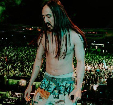 DJ Steve Aoki durante show em um palco com o público ao fundo