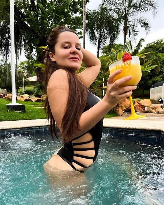 Maiara toma um drink na piscina enquanto olha para a câmera