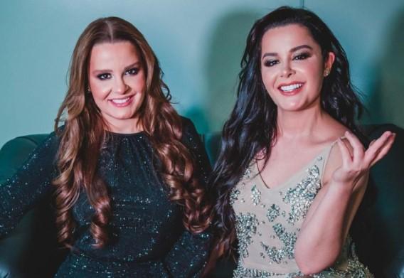 Maiara e Maraisa posam juntas sentadas em sofá e sorriem