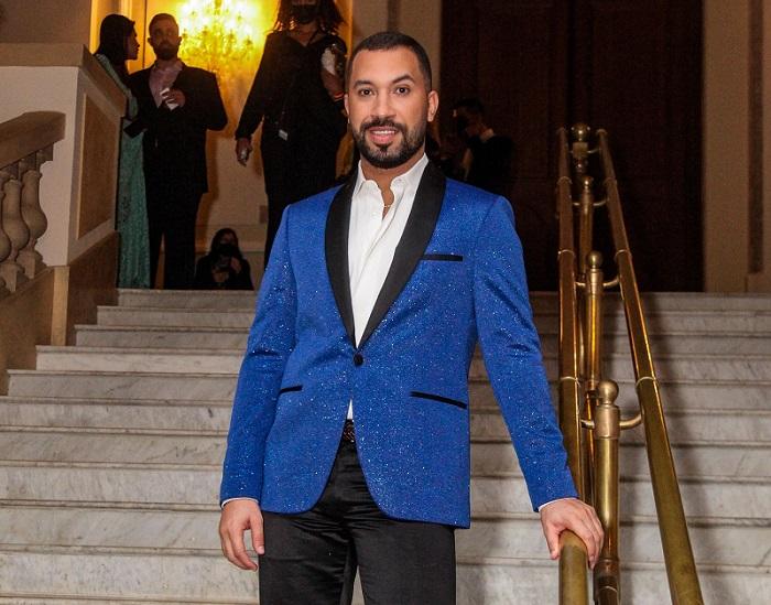 Gil posa para a foto em meio a uma escadaria branca, vestindo um blazer azul brilhante