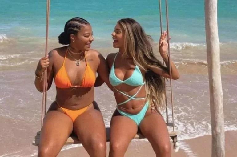 Brunna e Ludmilla sorriem, sentadas em um balanço no meio do mar.