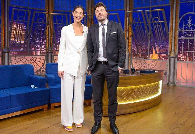 Lado a lado, Carol Gattaz e Danilo Gentili sorriem para foto no palco do The Noite