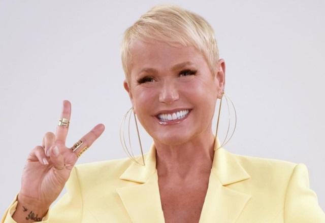 Xuxa Meneghel sorri para foto, fazendo sinal de paz e amor.