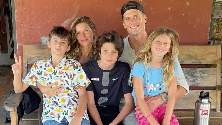  Gisele Bündchen e Tom Brady sentado no banco com as três crianças no colo.