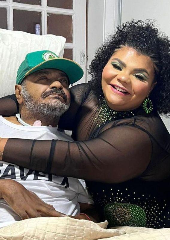 Flora Cruz posa abraçada com Arlindo Cruz, que está sentado na cama