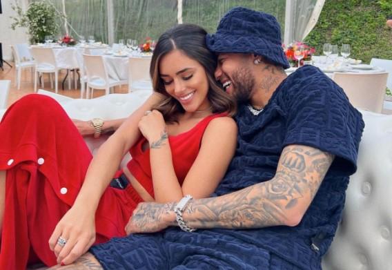 Neymar e Bruna Biancardi posam sentados sem sofá, abraçados e sorrindo um para o outro