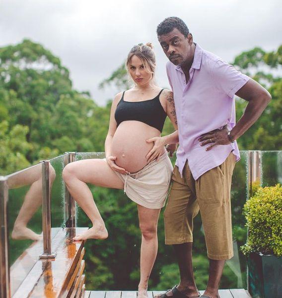 Seu Jorge e esposa grávida posam para foto em paisagem de floresta