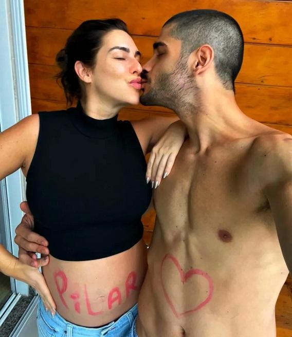 Fernanda Paes Leme e Victor Sampaio dando selinho enquanto posam com a barriga de Fepa, que está com o nome da filha escrito com tinta