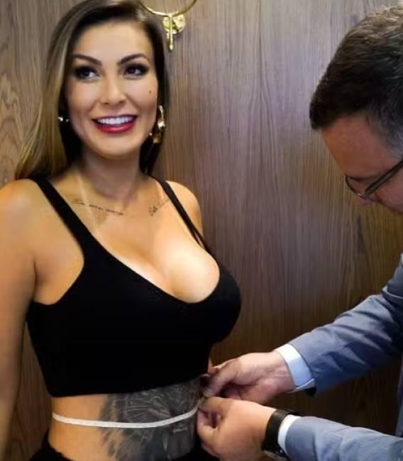 Andressa Urach posa sorrindo enquanto médico tira medida de sua cintura