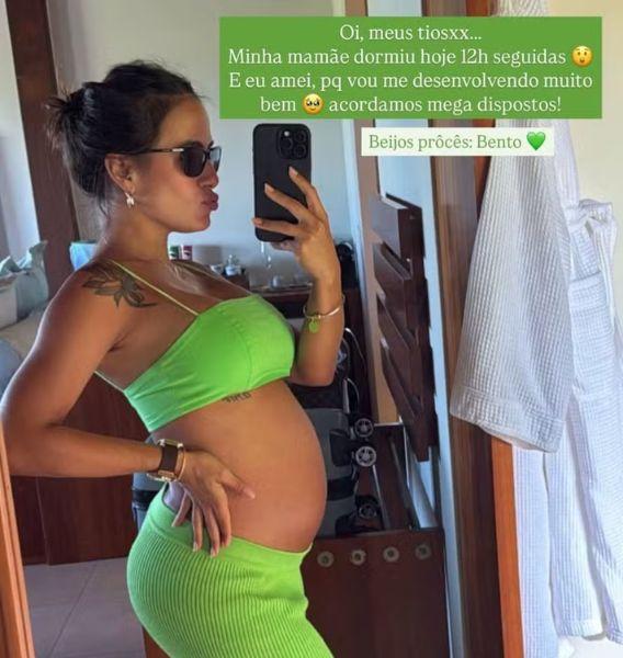 Carol Peixinho com top e saia verde, mostrando a barriguinha de grávida no espelho