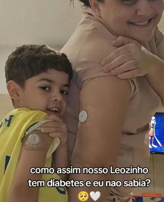 Léo e a babá aparecem juntos mostrando o sensor para monitorar a glicose