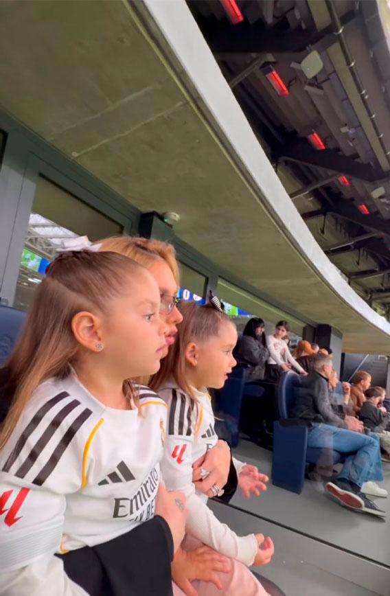 foto onde maria flor e maria alice aparecem com o uniforme do real madrid abraçadas com virginia no estádio