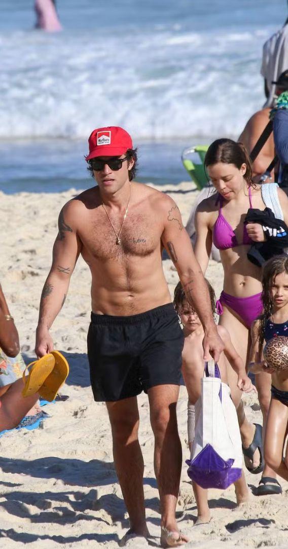 Chay Suede curte praia com os filhos. O ator apareceu ao lado daas crianças usando um boné vermelho, óculos escuros e sem camisa.